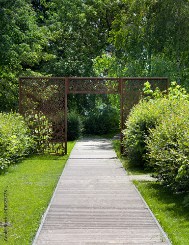 Road in the garden. Walk in the park. Garden path from the flooring. Openwork arch, pergola in the park.