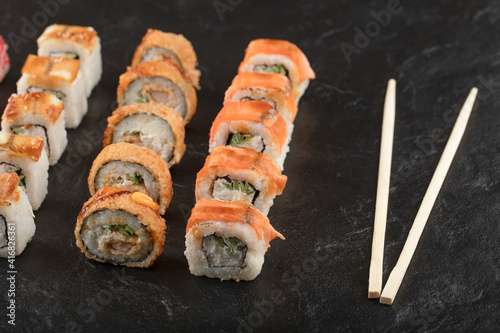 Set of delicious sushi rolls and chopsticks on black surface