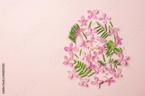 Happy Easter card. Easter egg shape made of pink flowers and green leaves on pink background. Flat lay pattern. Coppy space.