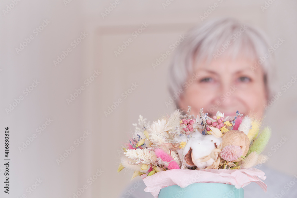 A portrait of an elderly Caucasian woman with short gray hair with a bouquet of dried flowers. A portrait of an elderly Caucasian woman with short gray hair with a bouquet of dried flowers.