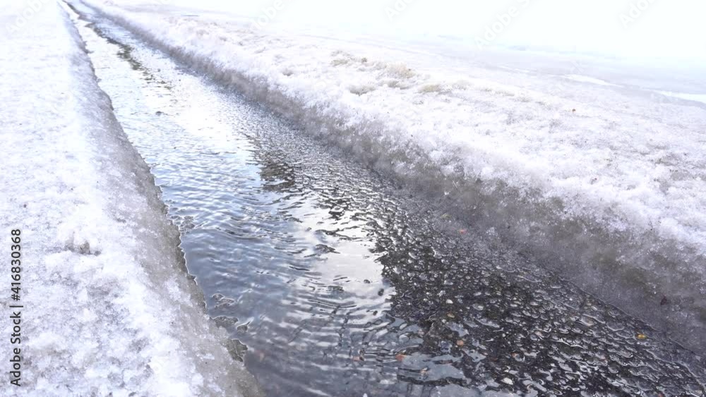 The spring stream flows on the asphalt, the snow melts and flows down the car track The spring stream flows on the asphalt, the snow melts and flows down the car track