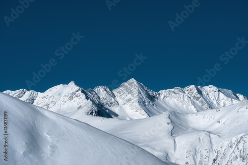 The Caucasus Mountains. The northern slope of the Arkhyz ski resort. Mountain terrain against a blue sky. Winter mountain landscape. Background, wallpaper. © mazurevanasta