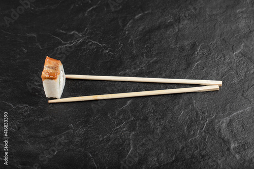 Single dragon sushi roll with chopsticks on black background