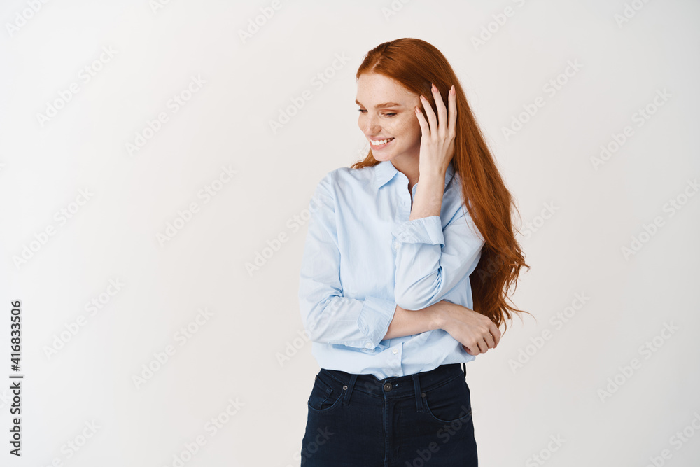 Beautiful woman with long red hair blushing and looking away shy, standing over white background and smiling Beautiful woman with long red hair blushing and looking away shy, standing over white background and smiling