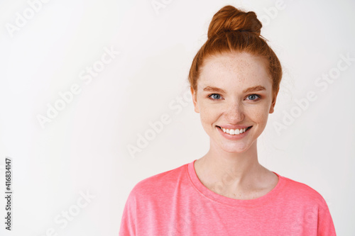 Skincare and makeup concept. Close-up of teen girl with red hair and freckles, showing glowing skin with natural makeup, smiling at camera