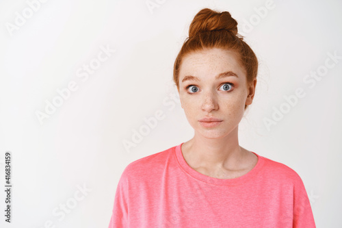 Skincare and makeup concept. Close-up of clueless young redhead woman acting confused, staring with blue eyes at camera and shrugging, standing over white background