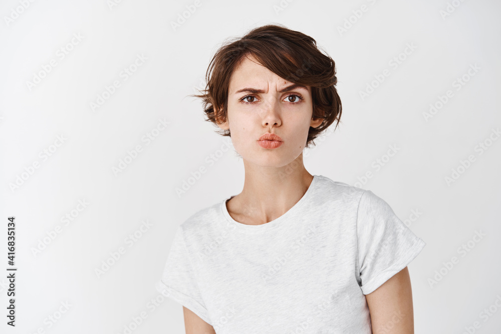 Skeptical caucasian woman look perplexed at camera, pucker lips and raising eyebrow suspicious, feeling doubtful or unsure, standing on white background Skeptical caucasian woman look perplexed at camera, pucker lips and raising eyebrow suspicious, feeling doubtful or unsure, standing on white background