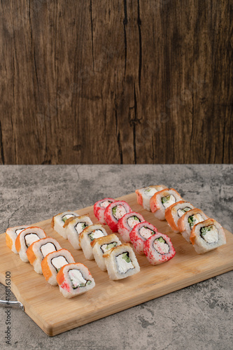 Wooden board of various sushi rolls on marble table