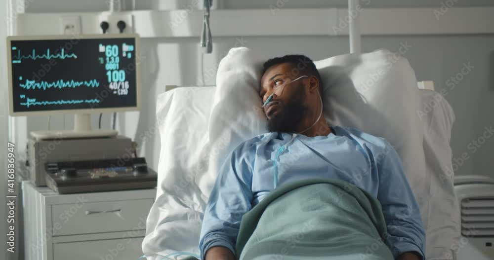 Seriously ill african man lying on bed in hospital with monitors showing his vital signs.