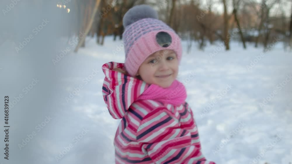 Smiling child kid throws snowball into camera in winter park forest. Portrait of cute girl having fun, throwing snowflakes, fooling around outdoors in frosty day. Children at Christmas holidays time Smiling child kid throws snowball into camera in winter park forest. Portrait of cute girl having fun, throwing snowflakes, fooling around outdoors in frosty day. Children at Christmas holidays time