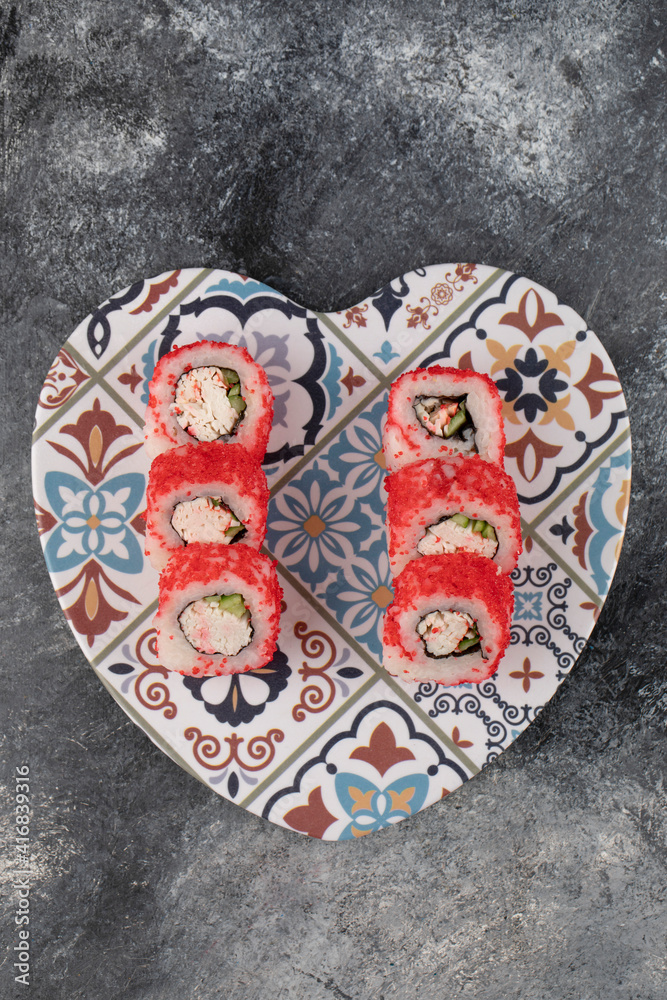 Tasty sushi rolls with red caviar on heart-shaped plate