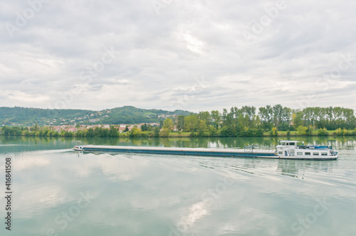front view, far distance of a river barge moving on the Rhone river, on a cloudy, rainy day 