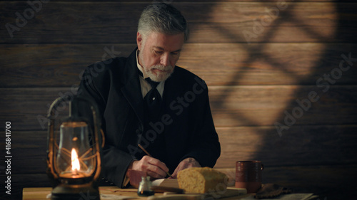 фотографія 19th century rustic scene of a gentleman writing in journal using dip pen with breakfast on the table
