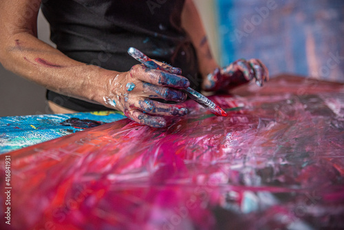 Young woman paints an abstract picture with her hands in her interior studio, focus on hand
