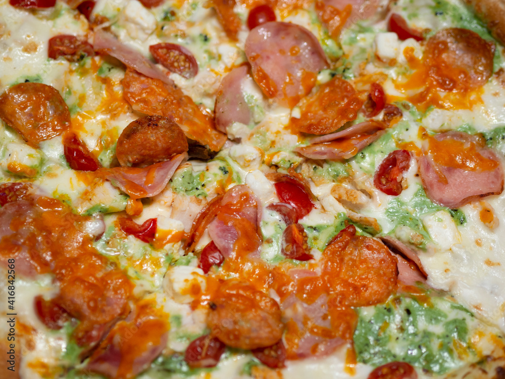 Traditional Italian fast food. Pizza with green pesto sauce, bacon, sausage, meat, ham, chicken, tomatoes, cheese, herbs and spices on a thin dough with sides. The concept of obesity, unhealthy food.