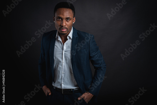 Portrait of attractive, handsome, cute, serious and stylish professional african american businessman executive with stylish suit and white shirt isolated on dark background. Low key. Selective focus