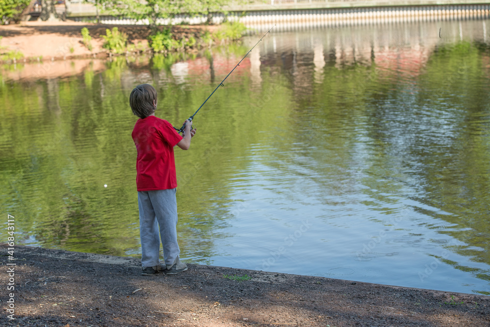 Young boy wearing a red shirt, casting a fishing pole into a lake. 