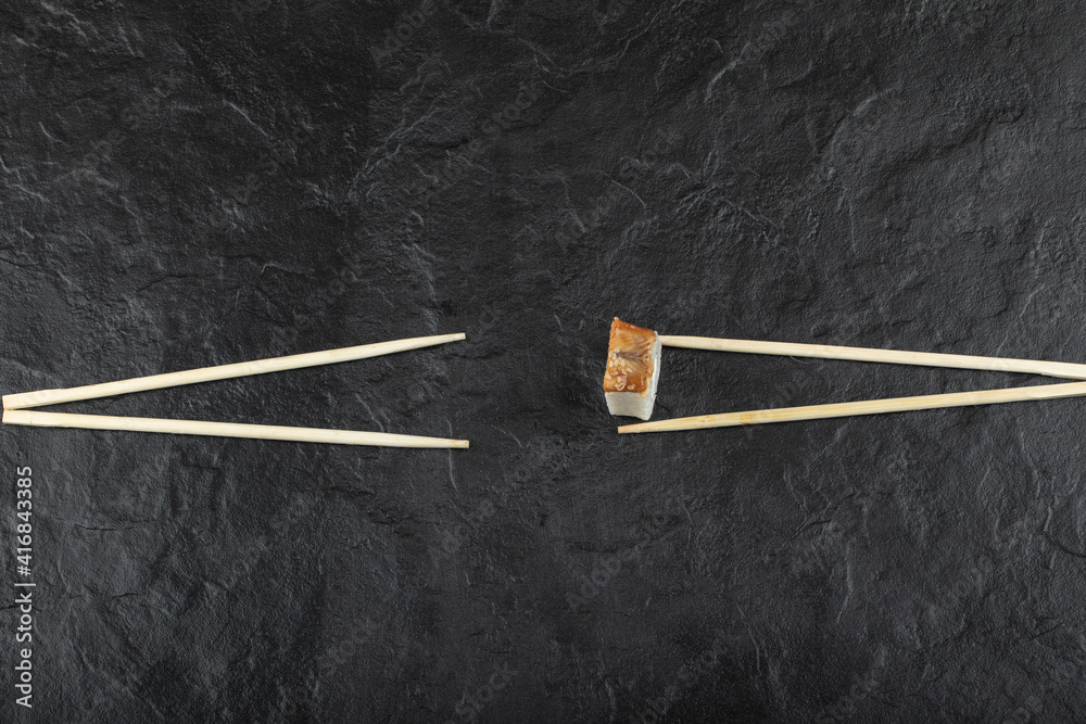 Single dragon sushi roll with chopsticks on black background