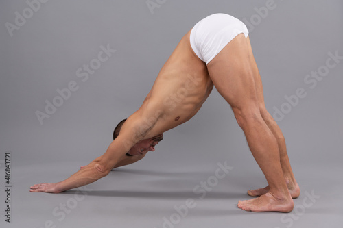 Yogi man do downward dog Adho Mukha Svanasana yoga standing pose grey background, asana photo