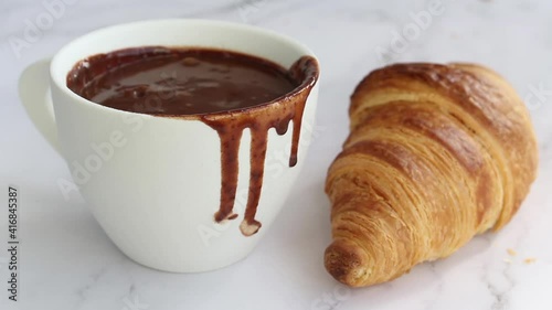 Pouring hot chocolate on white cup. with french croissant on table