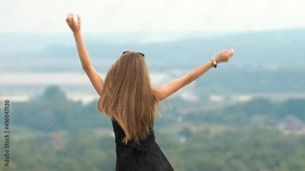Back view of a young energetic woman with long hair in short summer dress dancing happily in nature outdoors. Back view of a young energetic woman with long hair in short summer dress dancing happily in nature outdoors.