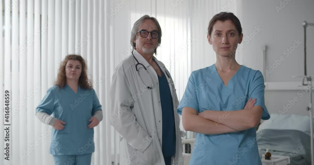 Team of medical professionals looking at camera standing in hospital ward Team of medical professionals looking at camera standing in hospital ward