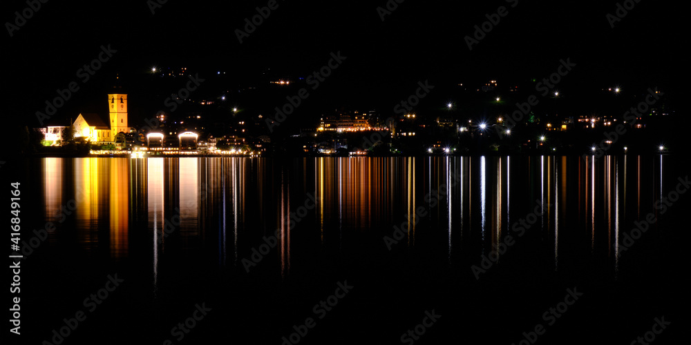 House lights of St Wolfgang im Salzkammergut village, with reflections in the water, at night. Austria, tourism.