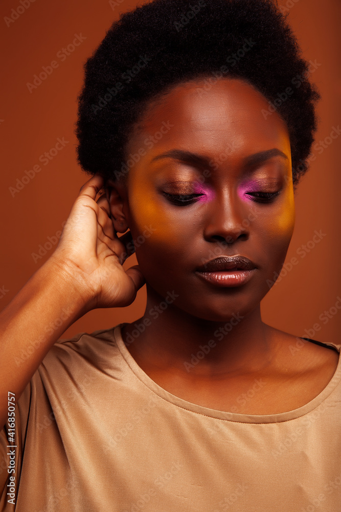 pretty young african american woman with curly hair posing cheerful gesturing on brown background, lifestyle people concept