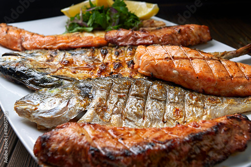Grilled fish on a white plate with herbs and lemon, dorado, mackerel, salmon steak, salmon fillet, on a wooden board