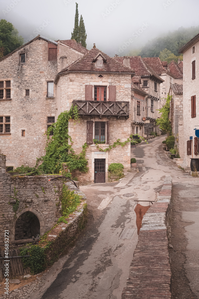 The quaint and charming French medieval hilltop village of Saint-Cirq-Lapopie on a foggy, misty morning in the Lot Valley, France.