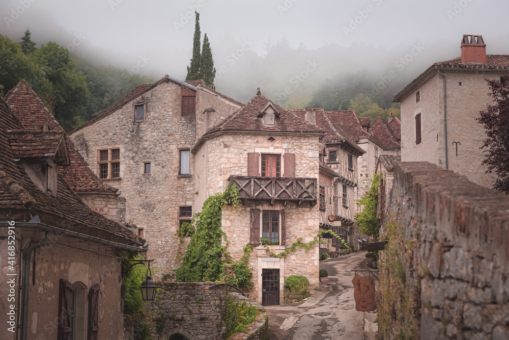 The quaint and charming French medieval hilltop village of Saint-Cirq-Lapopie on a foggy, misty morning in the Lot Valley, France.