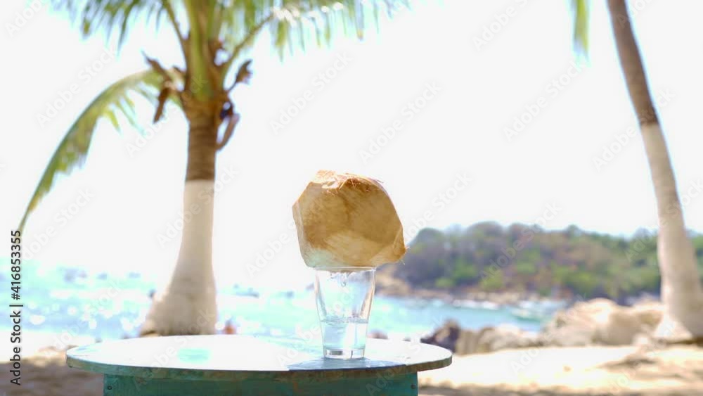 the coconut is on the glass dropping the water into the glass, on a paradise beach with palm trees. ideal for advertising cocktails. with copy space for your promotional content the coconut is on the glass dropping the water into the glass, on a paradise beach with palm trees. ideal for advertising cocktails. with copy space for your promotional content