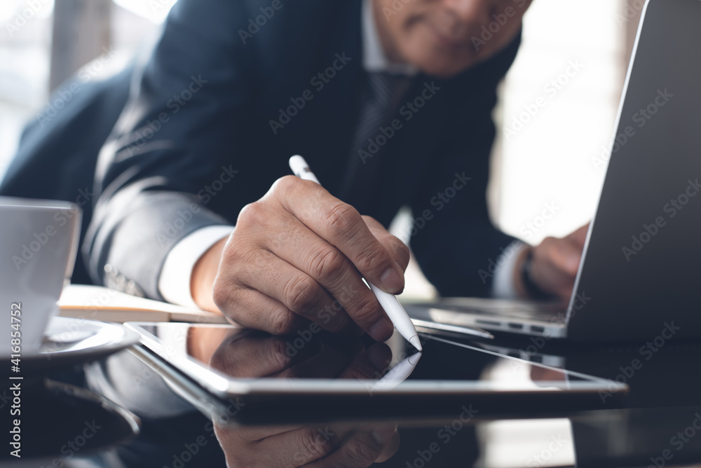 Businessman using touchscreen pen on digital tablet and working on laptop computer at modern office Businessman using touchscreen pen on digital tablet and working on laptop computer at modern office