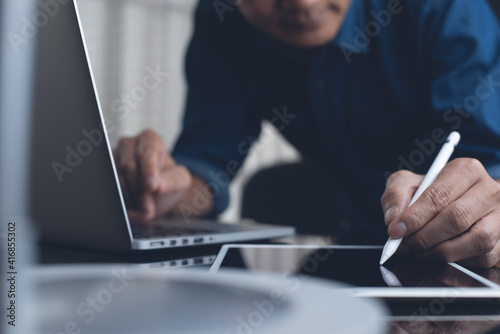 Man using touchscreen pen on digital table and working on laptop computer on office table