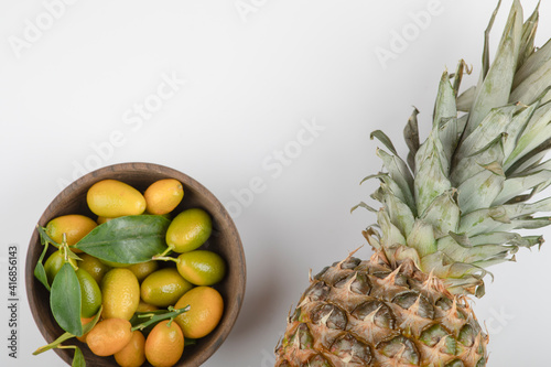 Wooden bowl of yellow kumquats and pineapple on white background