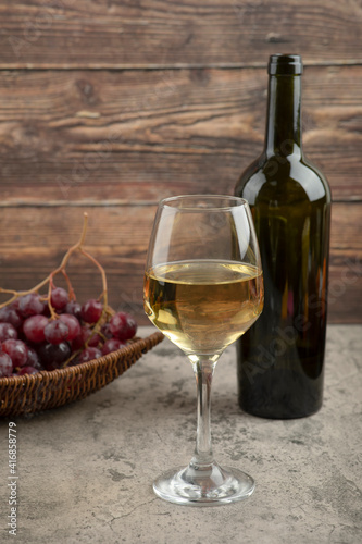 Wicker basket of red grapes with glass of white wine on marble table