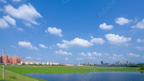 City buildings and lake view in the park under blue sky and white clouds