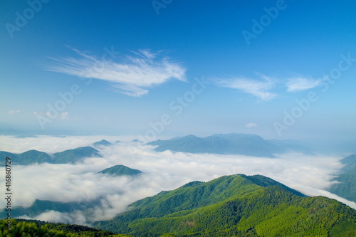 Top view of sea of clouds among green mountains and valleys, sunny blue sky background