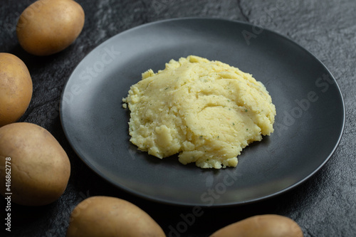 Close up of mashed potato on a plate, and fresh potatoes around it