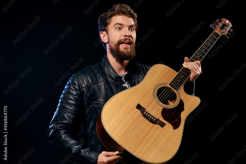 Obraz premium A man with a guitar in his hands leather jacket music performance rock star modern style dark background