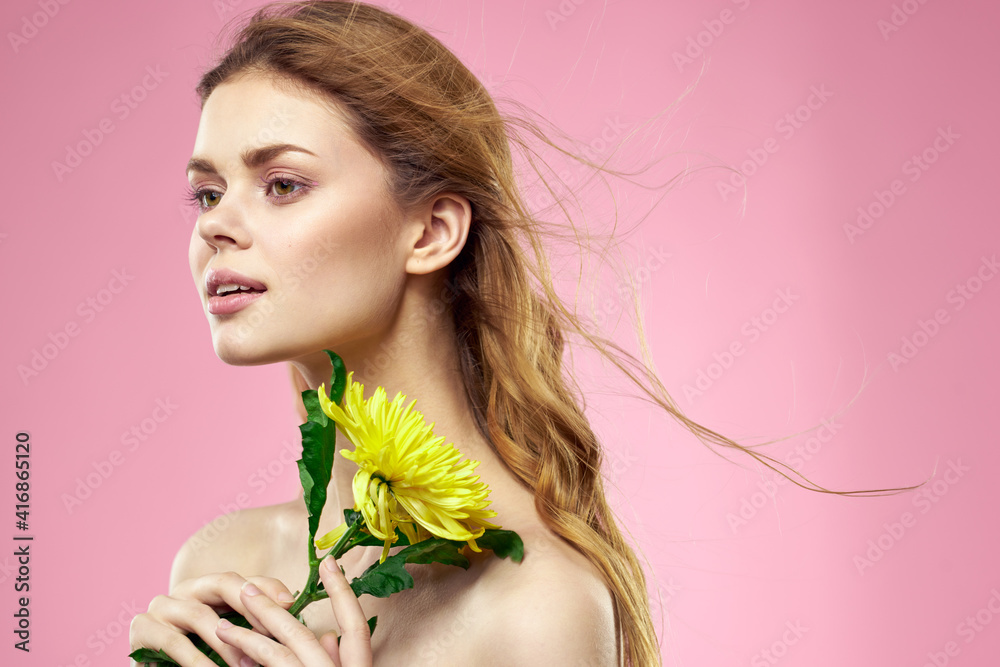 Fototapeta premium Beautiful girl with a yellow flower on a pink background nude shoulders makeup