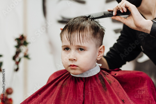 Close-up of woman hands grooming kid boy hair in barber shop.