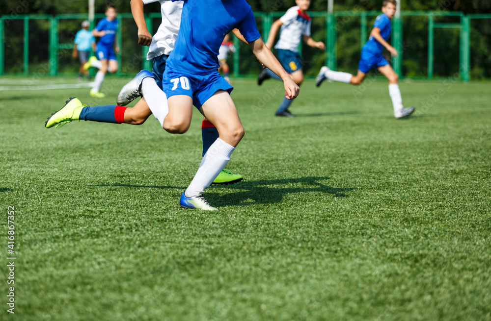 Young sport boys in blue sportswear running and kicking a  ball on pitch. Soccer youth team plays football in summer. Activities for kids, training	