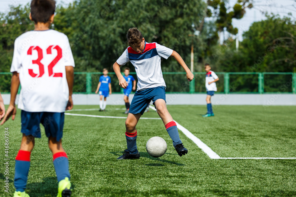 Young sport boys in blue sportswear running and kicking a ball on pitch. Soccer youth team plays football in summer. Activities for kids, training Young sport boys in blue sportswear running and kicking a ball on pitch. Soccer youth team plays football in summer. Activities for kids, training
