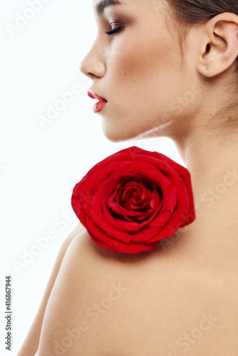 Nude brunette woman with red flower on her shoulder and bright makeup