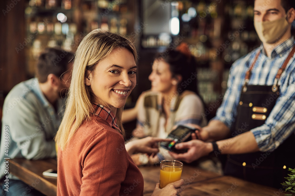 Happy woman paying bill in a pub and looking at camera. Happy woman paying bill in a pub and looking at camera.