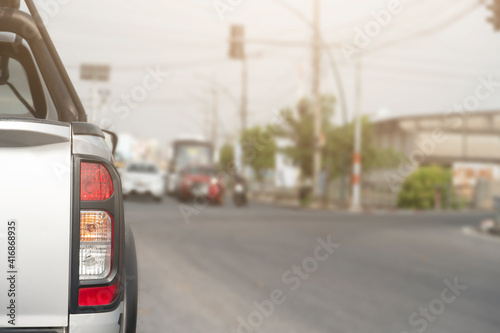 Back side of pick up car cilver color on the asphalt road with open brake light. Blurred vision of road traffic lights at the intersection.