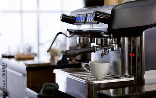 A white ceramic cup placed on the coffee maker. Prepare for making espressco coffee. Morning atmosphere in a coffee shop.