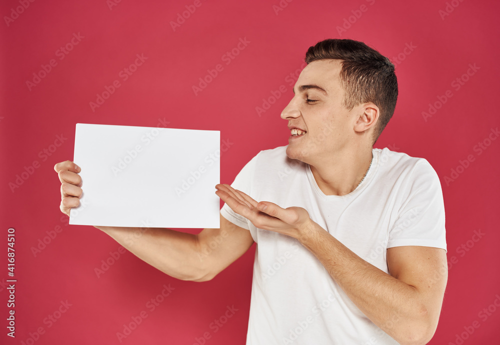 Puzzled young man on a red background are looking at a flyer in hand Puzzled young man on a red background are looking at a flyer in hand