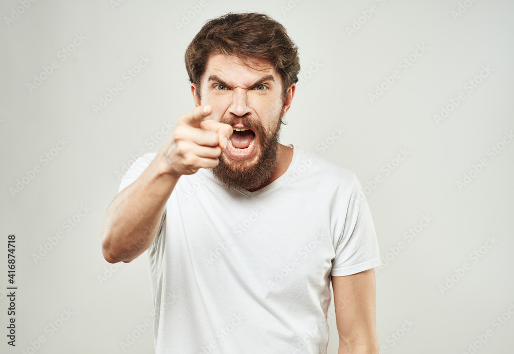 A guy in a white T-shirt gestures with his hands on a light background aggression irritability stress A guy in a white T-shirt gestures with his hands on a light background aggression irritability stress